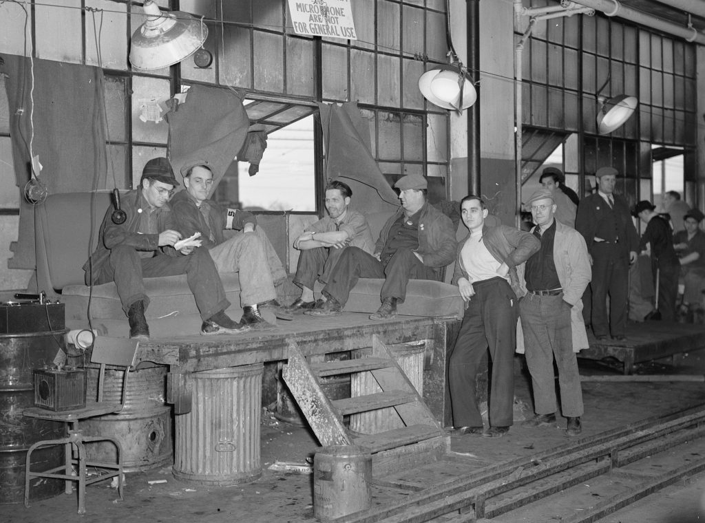 A group of men sitting outside a factory window during the Flint Sit-Down Strike. 